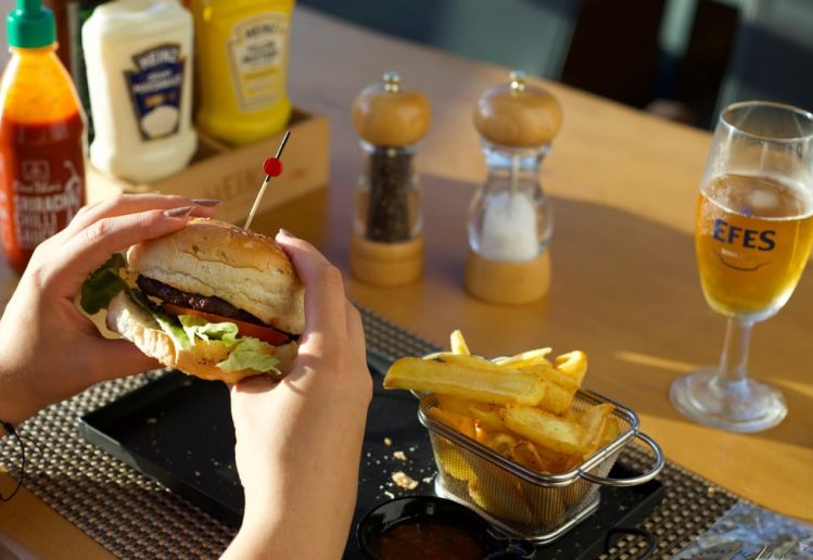A person enjoying a delicious burger and fries with a glass of beer at a restaurant.
