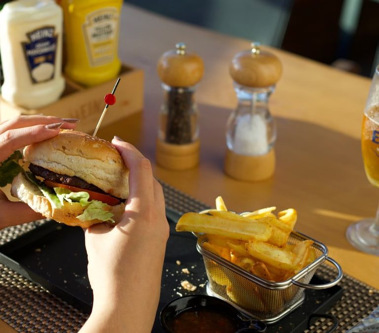 A person enjoying a delicious burger and fries with a glass of beer at a restaurant.