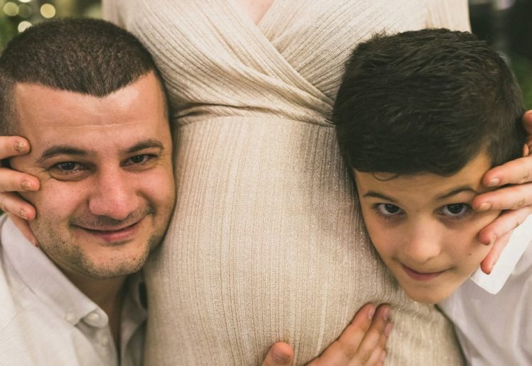 A joyful family moment with father and son embracing the pregnant mother, symbolizing love and togetherness.
