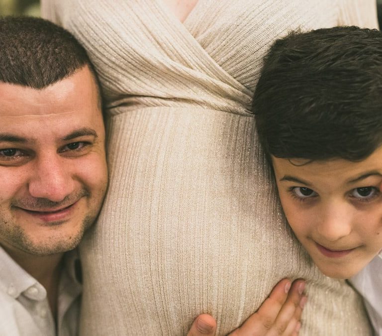A joyful family moment with father and son embracing the pregnant mother, symbolizing love and togetherness.