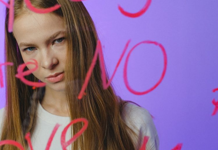 Teen girl with thoughtful expression behind written glass, moody studio shot.