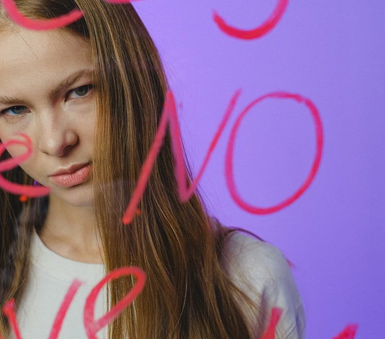 Teen girl with thoughtful expression behind written glass, moody studio shot.